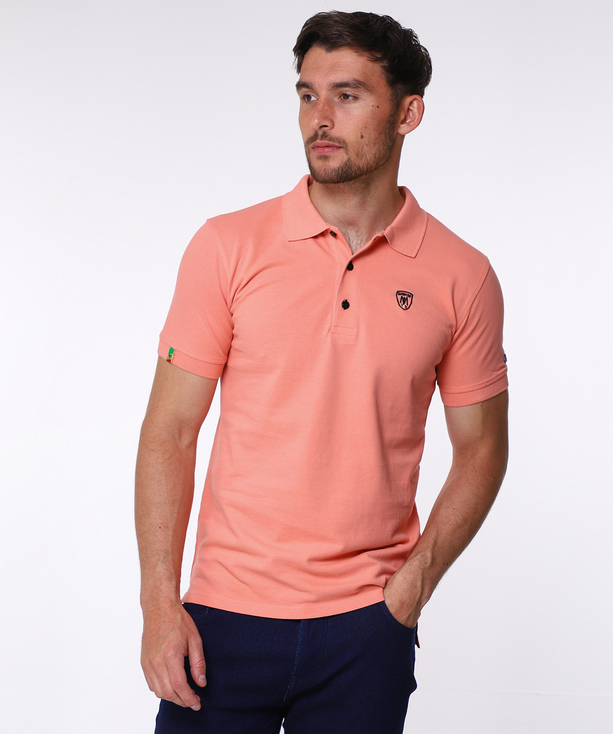Burnt Coral pique cotton round polo shirt, with small shield MANCINI logo on the chest and a small logo on the left arm. Contrasting black button hole stitching. The word MANCINI under the collar in black print. Red ribbon detail on the bottom inch of the t shirt on both sides.