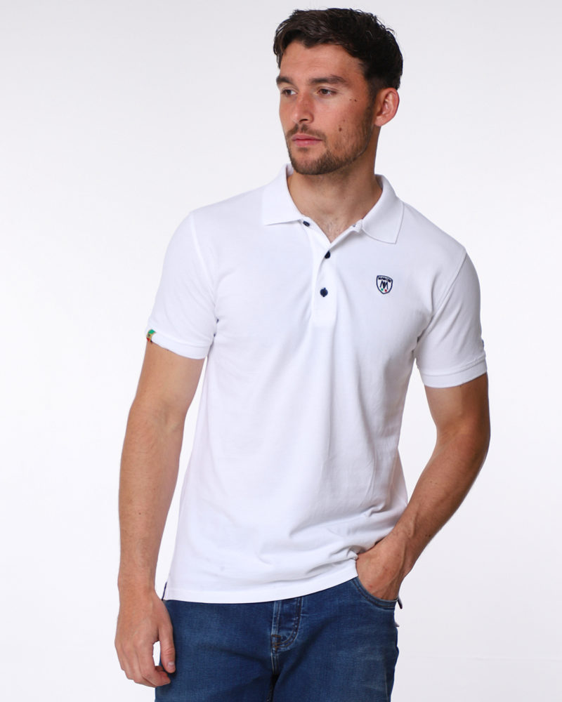 White pique cotton round polo shirt, with small shield MANCINI logo on the chest and a small logo on the left arm. Contrasting black button hole stitching. The word MANCINI under the collar in black print. Red ribbon detail on the bottom inch of the t shirt on both sides.